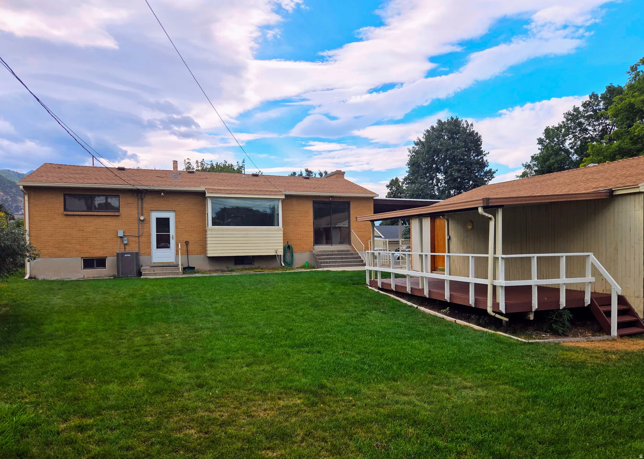 Expansive lawn area with a brick exterior, a large bay window, and a covered deck with railing