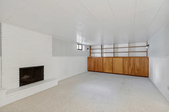 White-painted brick fireplace with a hearth, built-in wooden cabinetry with shelving, wall-mounted light fixtures, and neutral carpeting
