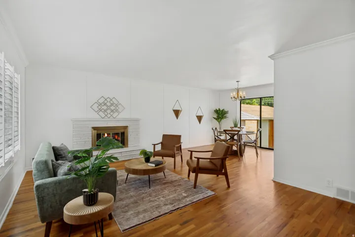 Hardwood flooring, white brick fireplace, crown molding, plantation shutters, and a dining area with a chandelier