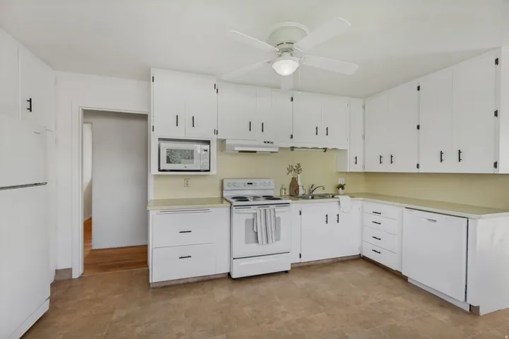 Kitchen featuring white cabinetry with black hardware, white appliances, a built-in microwave, and a ceiling fan with integrated lighting