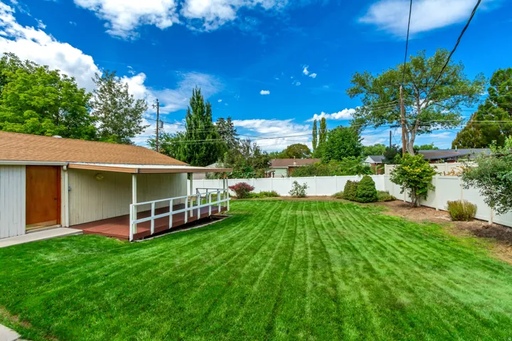 Expansive backyard with a manicured lawn, white privacy fencing, and a covered deck
