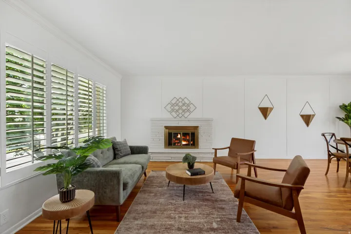 Hardwood flooring throughout, white plantation shutters, white brick fireplace, and crown molding