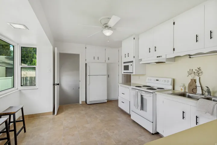 Kitchen featuring white cabinetry, neutral tile flooring, bay windows, white appliances, and a ceiling fan with integrated lighting