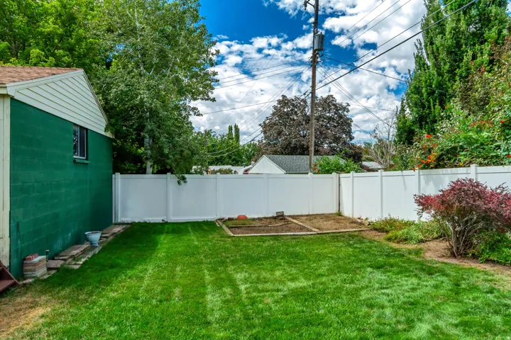Expansive green lawn, white vinyl fencing, dedicated garden bed, mature trees, and a detached structure with green siding