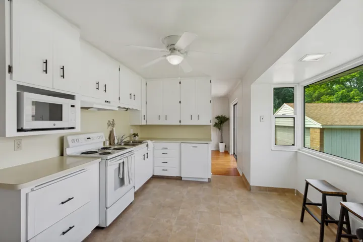 White cabinetry with black hardware, integrated microwave, tile flooring, and a large bay window