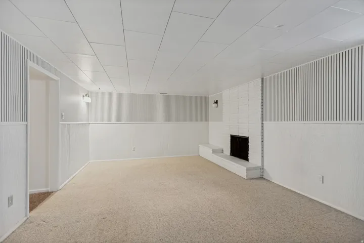 Painted brick fireplace with hearth, wall-mounted sconces, carpet flooring, and panel accent walls