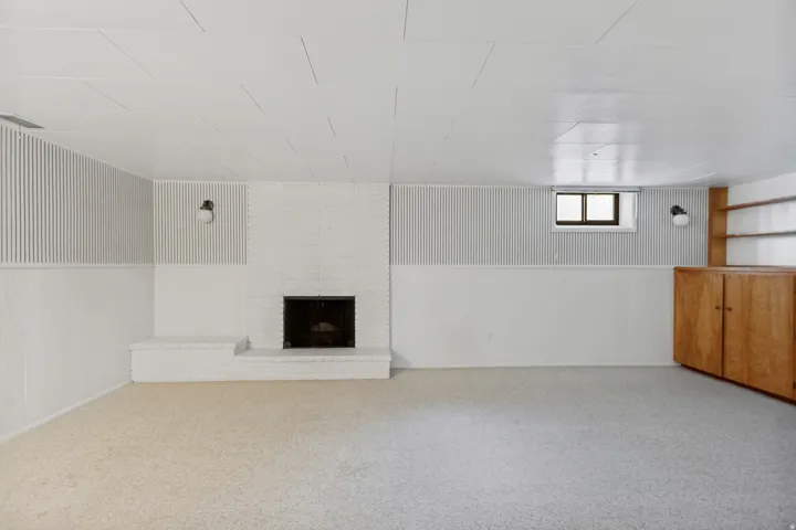 White-painted brick fireplace with an extended hearth, built-in wooden cabinetry, recessed window, and wall-mounted sconce lighting