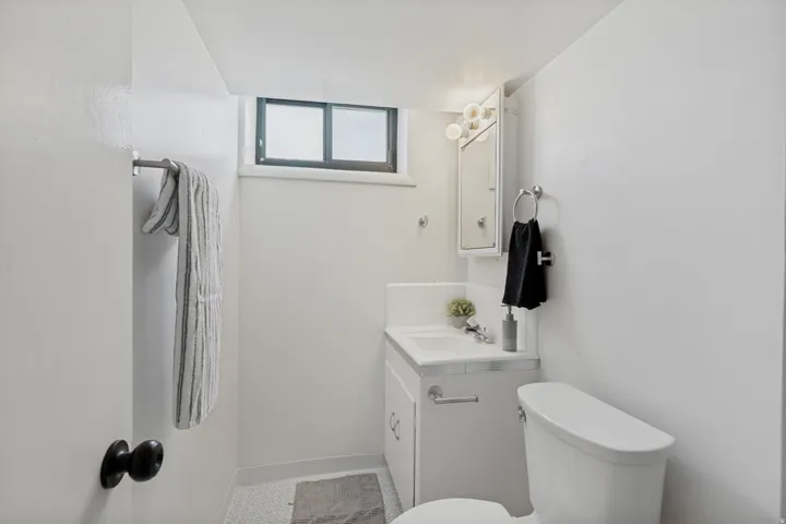 Compact bathroom featuring a window, vanity with integrated sink, wall-mounted medicine cabinet, white toilet, and hexagonal tile flooring