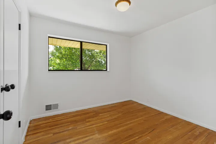 Hardwood flooring, white painted walls, window with black trim, and a ceiling-mounted light fixture