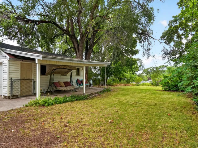 Covered patio with a concrete slab, expansive lawn, mature trees, and established landscaping