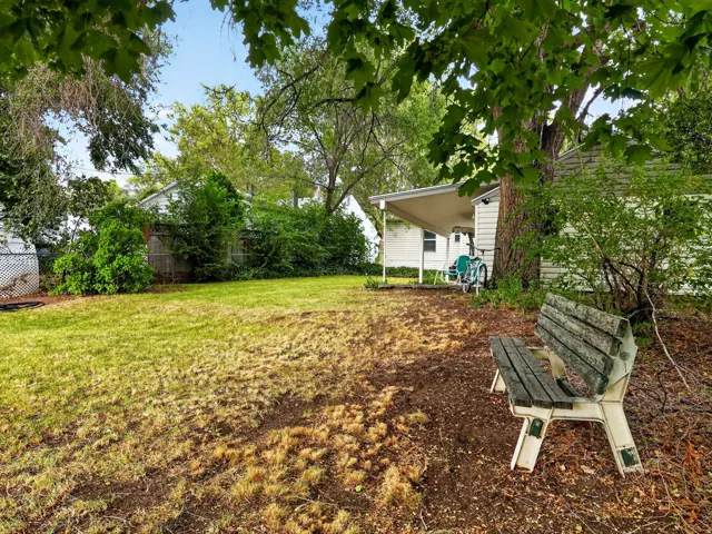 Expansive backyard featuring a manicured lawn, established trees, and a covered patio area