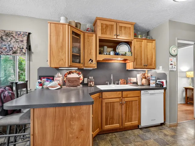 Kitchen featuring natural wood cabinetry, a built-in dishwasher, a double basin sink, and a peninsula with countertop seating