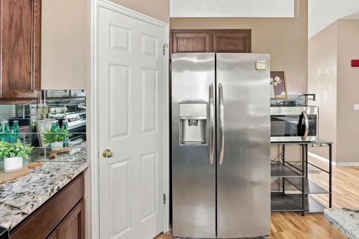 Stainless steel side-by-side refrigerator, speckled countertop, mirrored subway tile backsplash, dark wood-finish cabinetry, and paneled door