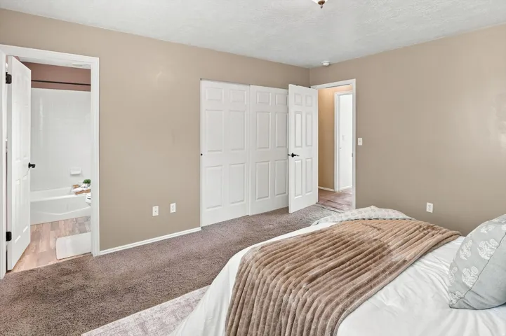 Primary bedroom.  Neutral wall tones, white bi-fold closet doors, and an en-suite bathroom featuring a tub/shower combination with white subway tile surround and wood-look flooring