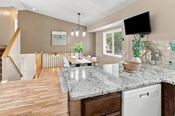 Angled ceiling with wood-finish flooring, kitchen island with stone countertop, wood cabinetry, and a dishwasher