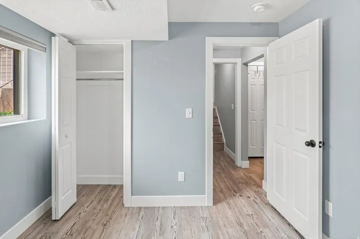 Wood-finish flooring, light blue painted walls, white trim, and a white six-panel door with black hardware
