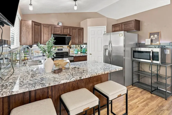 Kitchen featuring an island with stone countertops, dark wood-finish cabinetry, stainless steel appliances, and wood-finish flooring
