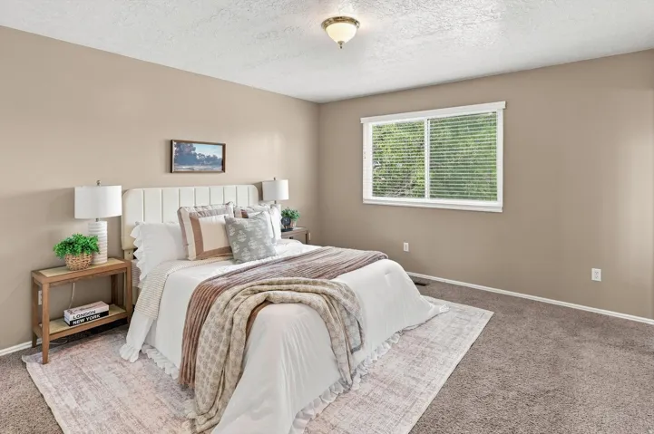 Room with textured carpet flooring, neutral-toned walls, and a white-framed window with blinds