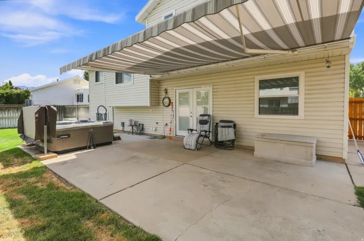 Concrete patio with retractable awning, featuring a hot tub, double glass doors