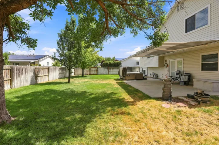 Expansive backyard featuring a concrete patio, mature trees, and a wooden privacy fence