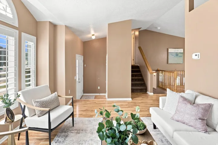 Multiple windows with white shutters, wood-finish flooring, vaulted ceiling, and staircase with wood railing