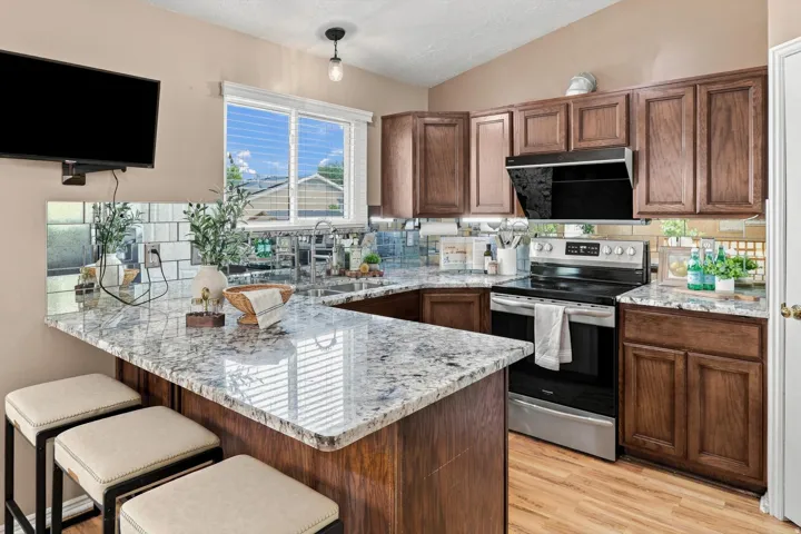 U-shaped kitchen featuring granite countertops, wood-finish cabinetry, a window over the sink, stainless steel appliances, Fotile vent, and a tile backsplash