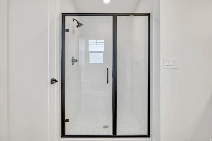 Frameless glass shower enclosure with matte black trim, featuring a rainfall showerhead and wall-mounted controls