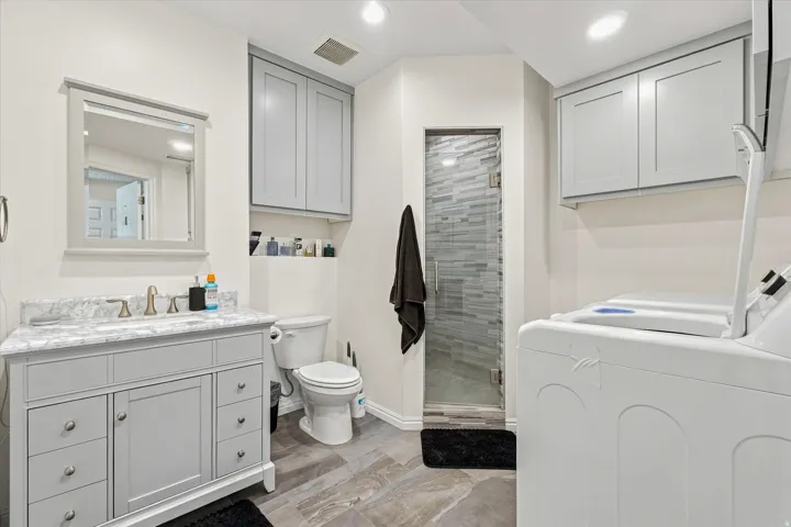 Gray vanity with a stone countertop, framed mirror, and a glass-enclosed shower featuring tiled walls