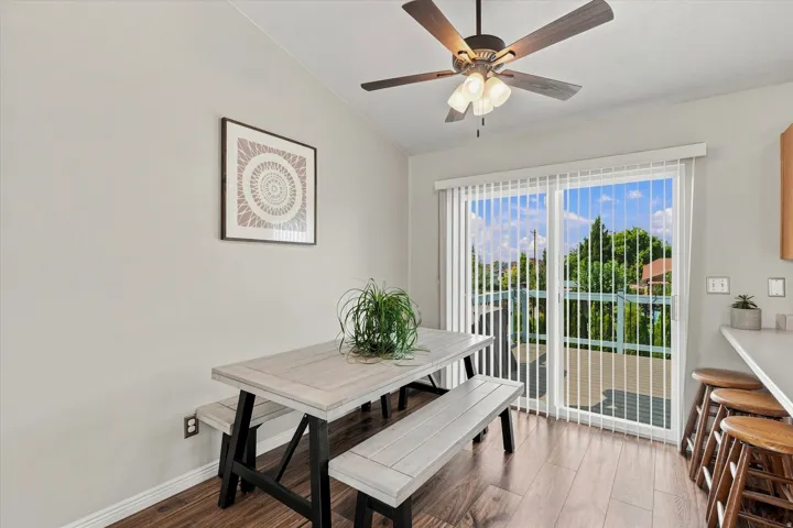 Sliding glass door, wood-finish flooring, ceiling fan with integrated lighting, white vertical blinds, and light-toned walls