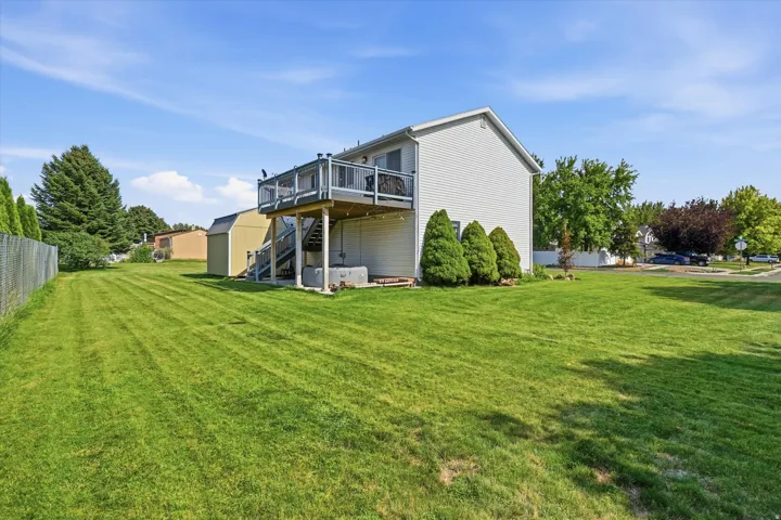Expansive green lawn, raised wood deck with railings, exterior siding, mature landscaping, and a detached shed