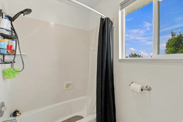 Bathtub with an integrated shower head, white surround, and a window with a roller shade
