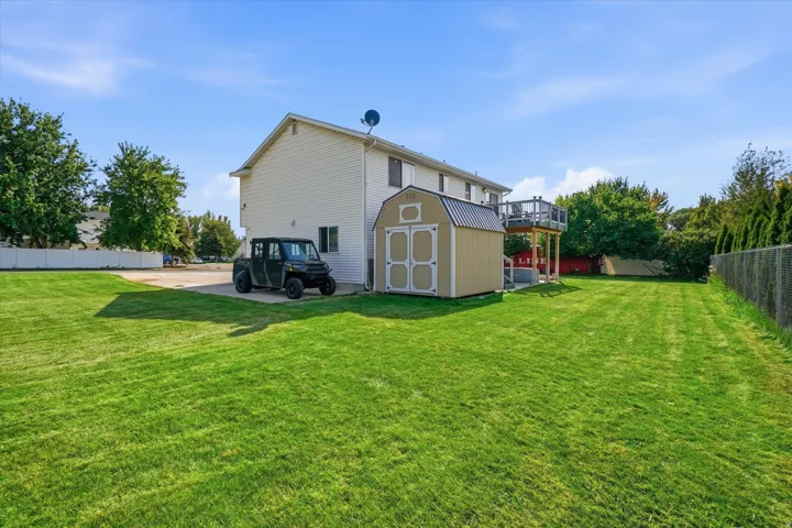 Expansive backyard featuring a manicured lawn, a detached storage shed, and an elevated wood deck