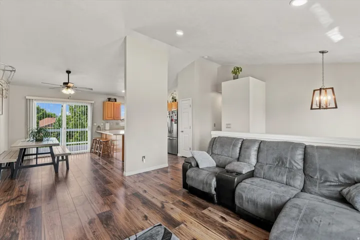 Wood-finish flooring throughout, recessed ceiling lighting, a ceiling fan with integrated lighting, and a sliding glass door with vertical blinds