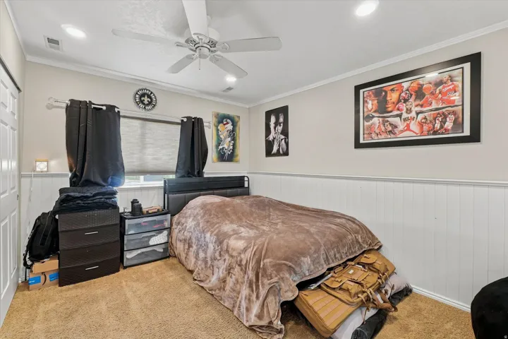 Carpeted room featuring white wainscoting, crown molding, and a ceiling fan with integrated lighting