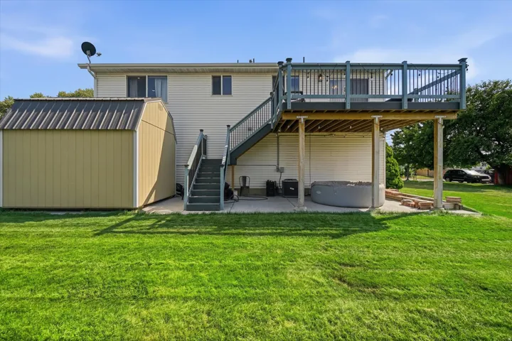 Expansive backyard featuring a manicured lawn, a detached storage shed with a metal roof, and a raised wooden deck with railings