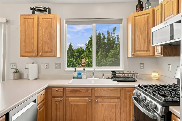 Kitchen with wood-finish cabinetry, solid surface countertops, a stainless steel gas range, and an over-range microwave