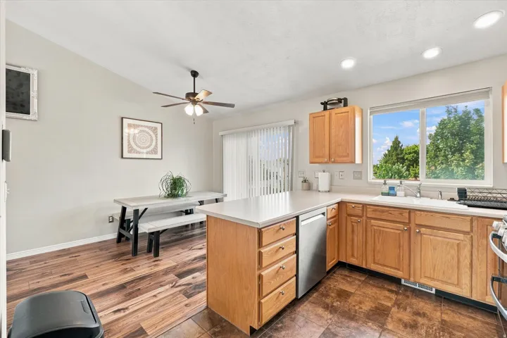 Kitchen featuring wood-finish cabinetry, light countertops, stainless steel dishwasher, and a window above the sink
