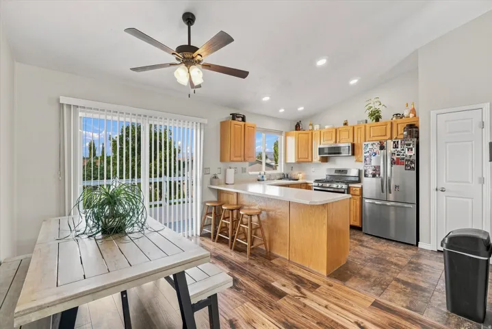 Kitchen and dining area featuring wood-finish flooring, light wood cabinetry, white countertops, stainless steel appliances, and a sliding glass door