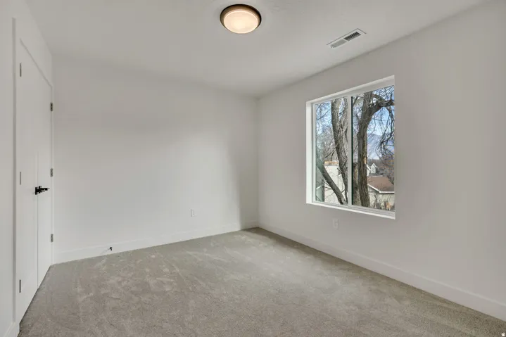 Bright secondary bedroom featuring carpet flooring, large window with natural light, and ceiling-mounted fixture