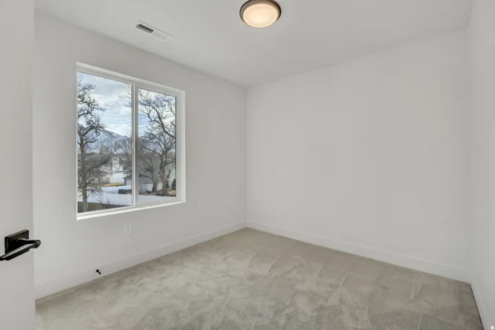 Bright corner bedroom featuring large dual-pane windows with natural light, neutral carpet flooring, and recessed ceiling lighting