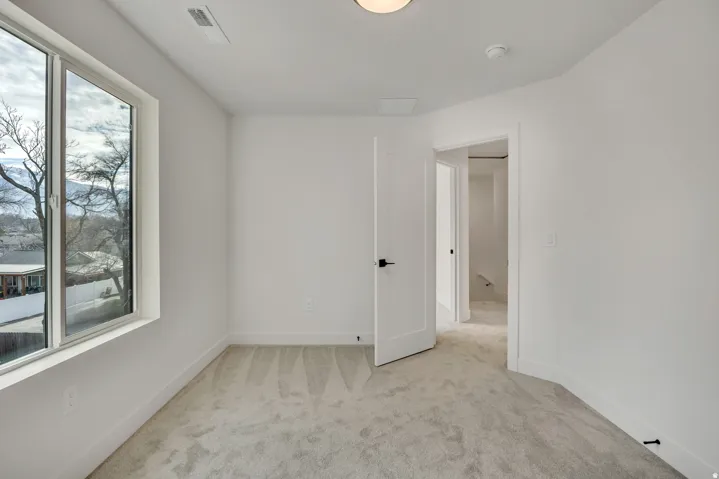 Bright corner bedroom featuring expansive windows with natural light, wood-finish flooring, and direct access to an ensuite bathroom