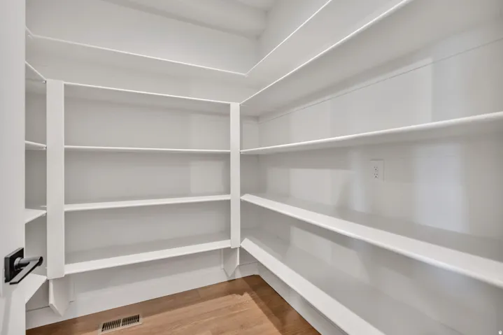 Spacious pantry featuring floor-to-ceiling white cabinetry with multiple shelves, recessed ceiling lighting, and wood-finish flooring throughout