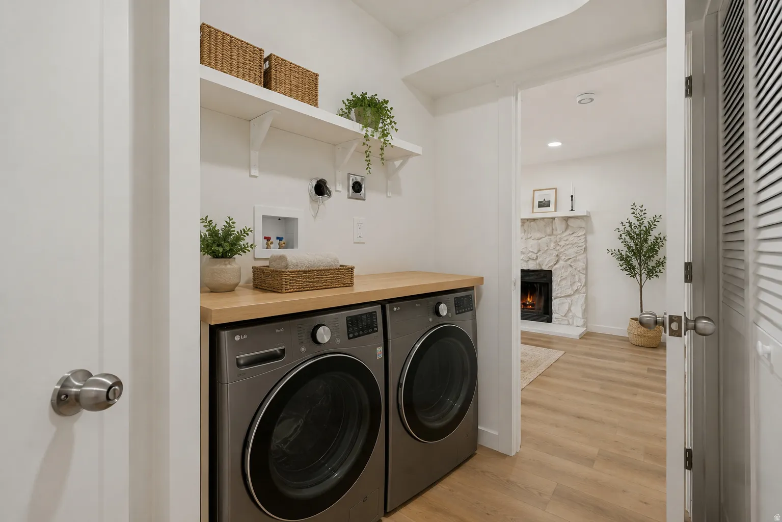 Dedicated laundry area with a wood-finish countertop, dual open shelving, and light wood-finish flooring