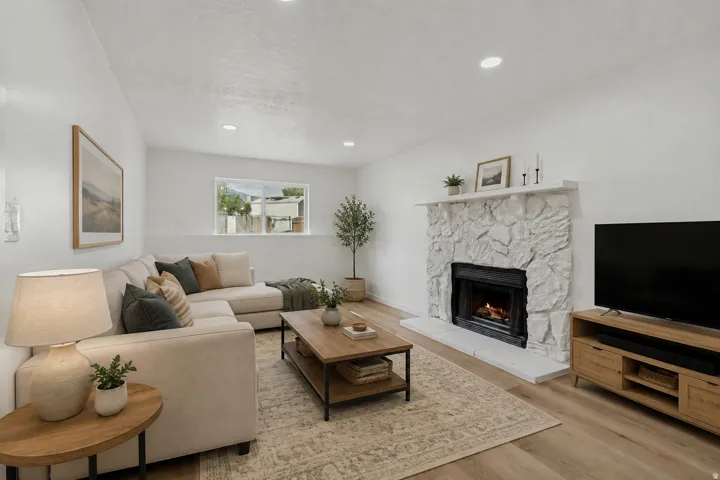 Living area featuring wood-finish flooring, recessed lighting, a stone fireplace, and a large window