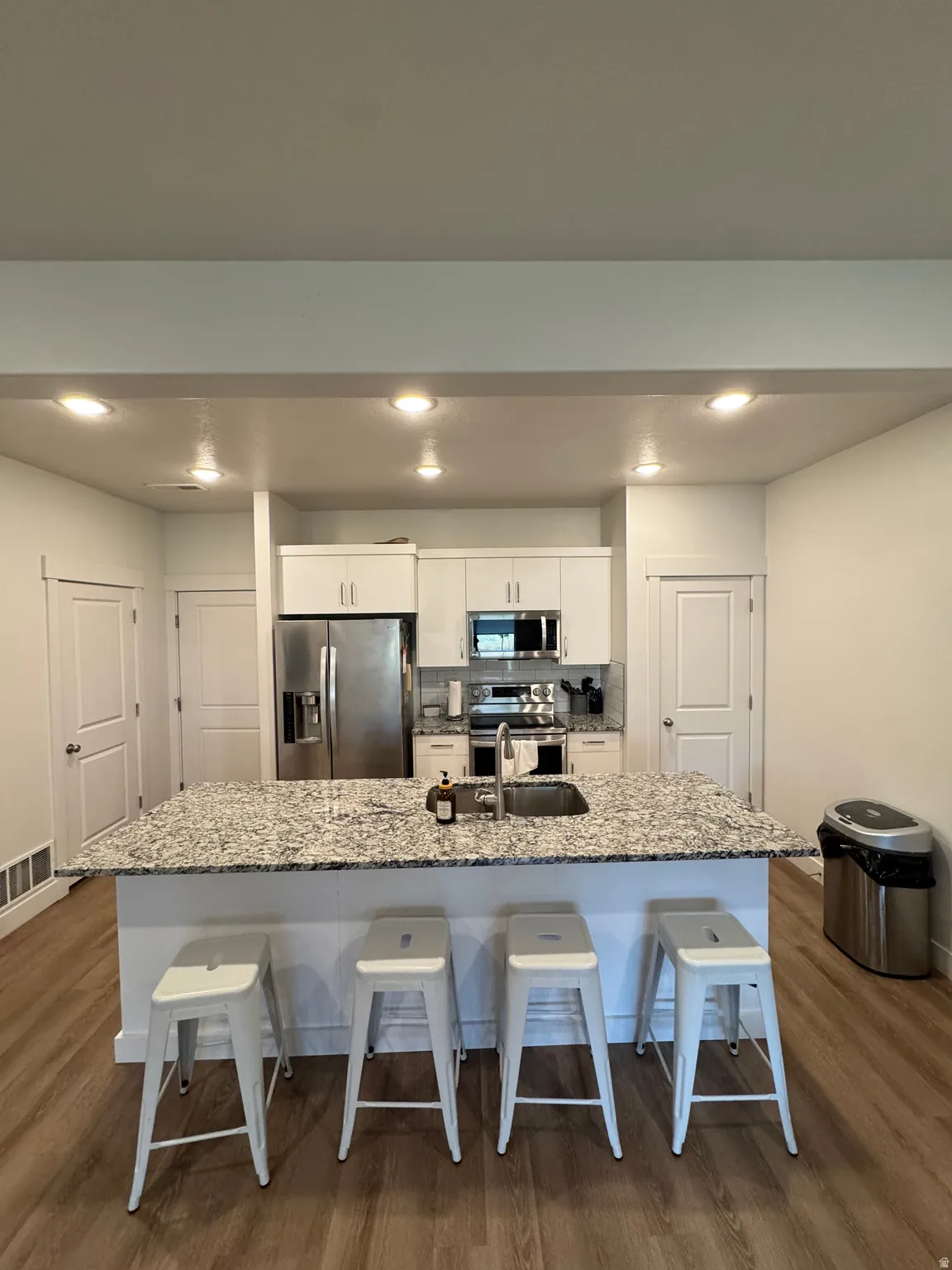 Kitchen featuring an expansive island with a built-in sink, white cabinetry, recessed lighting, stainless steel appliances, and wood-finish flooring