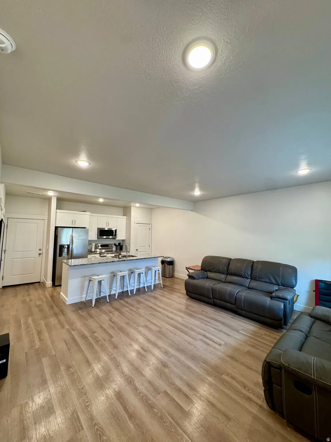 Open concept living area with wood-finish flooring, recessed lighting, white cabinetry, and stainless steel appliances