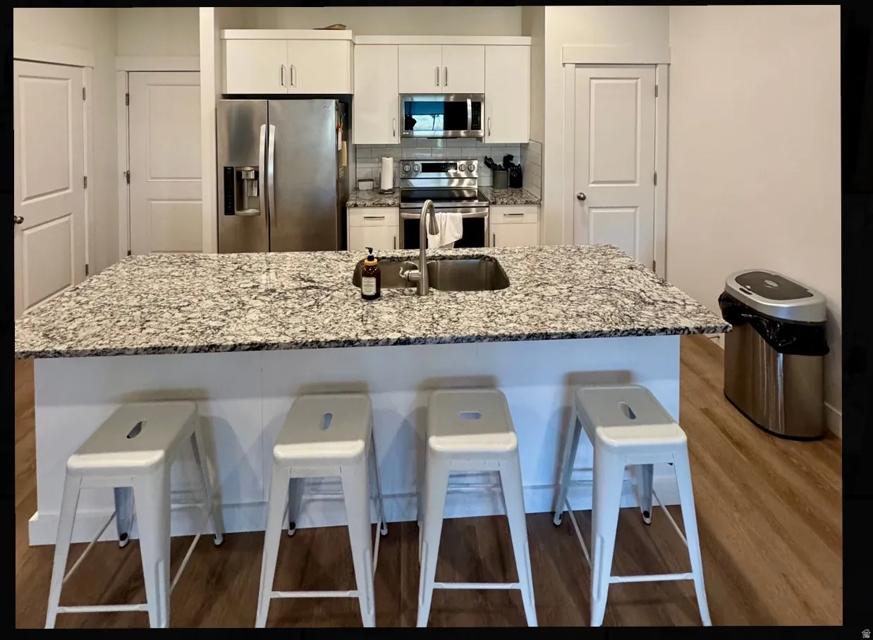 Kitchen featuring an expansive island with a stone-finish countertop, stainless steel appliances, white cabinetry, and wood-finish flooring