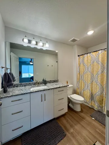Vanity with granite-style countertop, white cabinetry with brushed nickel hardware, expansive wall mirror, and wood-finish flooring