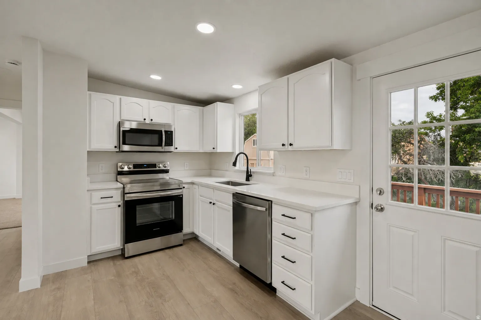 White shaker cabinetry, stainless steel appliances, wood-finish flooring, recessed lighting, and a paneled exterior door