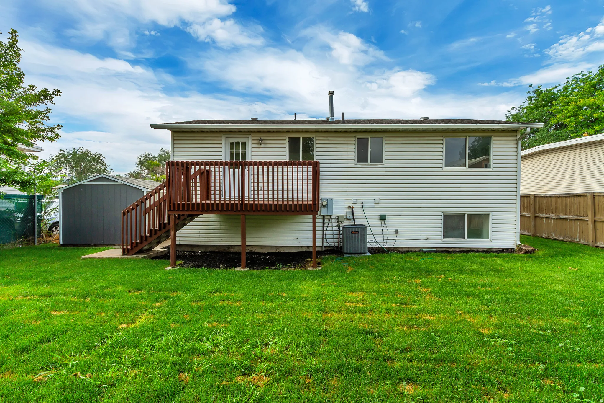 Rear exterior featuring a wood deck with stairs, white siding, and a detached storage shed